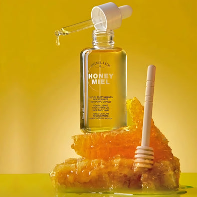 Bottle of Honey Miel Revitalizing Treatment Oil with a dropper on honeycomb against a yellow background