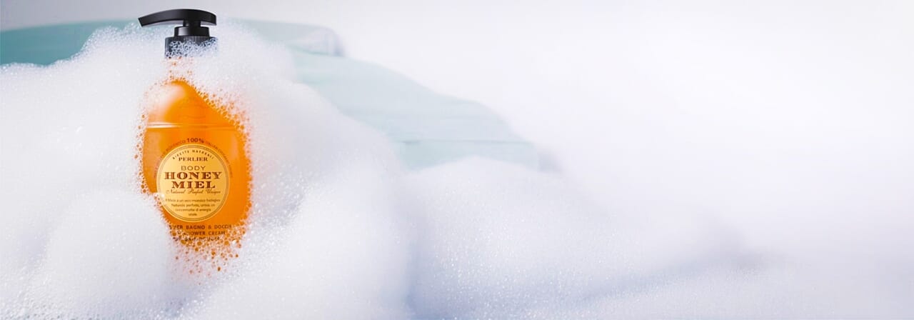 Bottle of Perlier Honey Mile Bath & Shower Cream in a bubble bath with a blue background