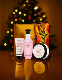 Perlier Pink Peony bath & body set on a reflective surface, Christmas tree in the background