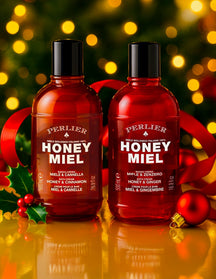 Two seasonally-scented bottles of Perlier Honey Miel Bath & Shower Creams with a festive background featuring lights and ribbons.