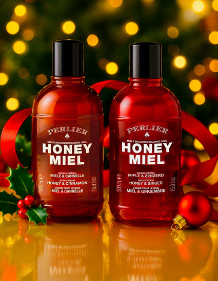 Two seasonally-scented bottles of Perlier Honey Miel Bath & Shower Creams with a festive background featuring lights and ribbons.