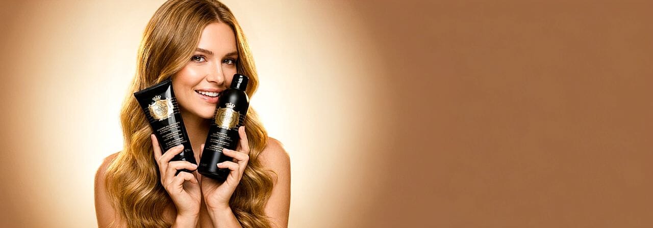 Woman holding two bottles of Perlier Imperial Honey hair care products against a beige background