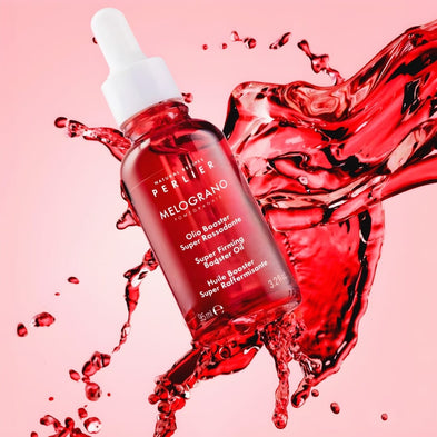 Perlier pomegranate booster oil bottle with red liquid splashes on a pink background