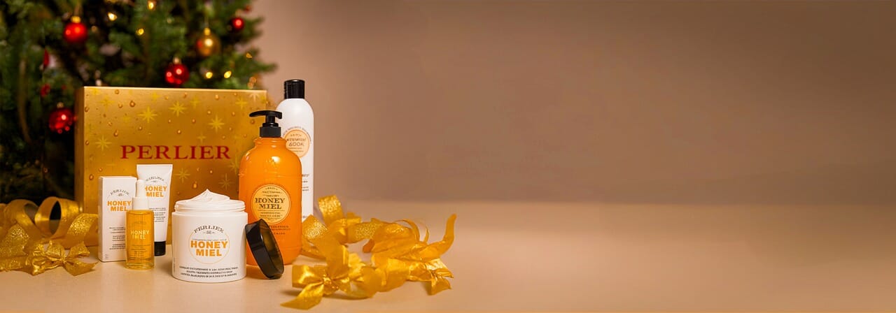 Perlier 5-pc holiday gift set - products and gift box on a beige background with a Christmas tree in the background