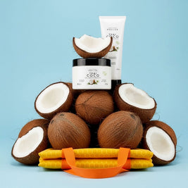 Perlier Thai Coco body cream and shower gel atop a pile of coconuts, and a yellow and orange tote bag on a blue background