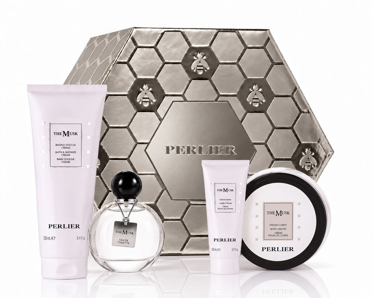 A holiday gift set from Perlier featuring The Musk products including a body wash, hand cream, body cream, and perfume arranged with a silver Perlier gift box, on a white background.