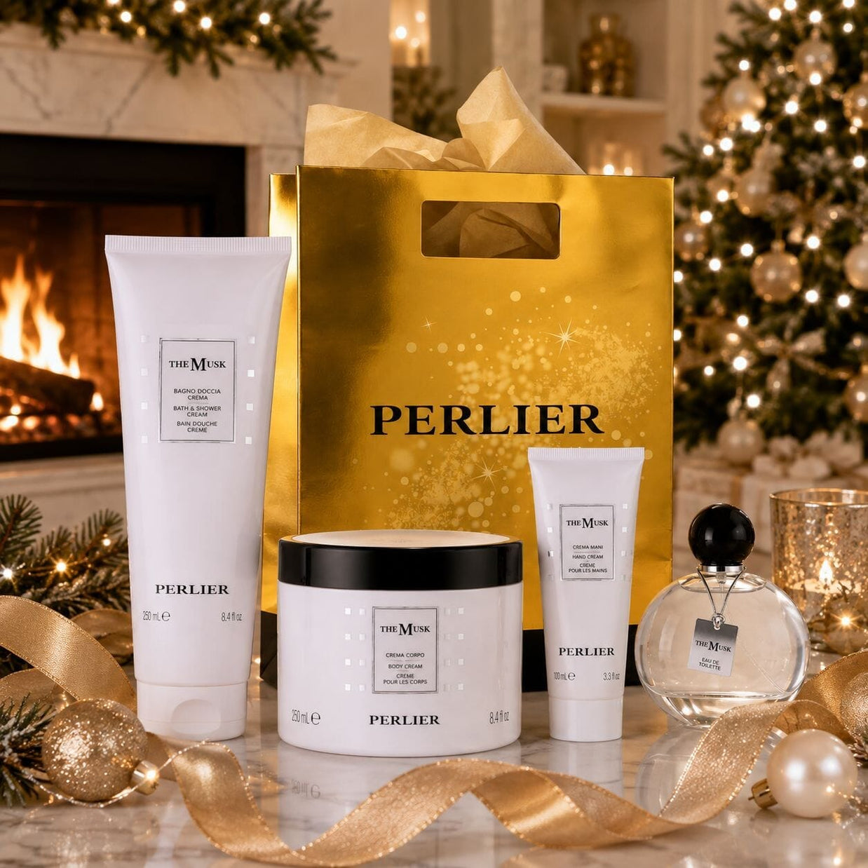 A holiday gift set from Perlier featuring The Musk products including a body wash, hand cream, body cream, and perfume arranged with a large gold Perlier shopping bag, and festive holiday decorations in front of a cozy fireplace.