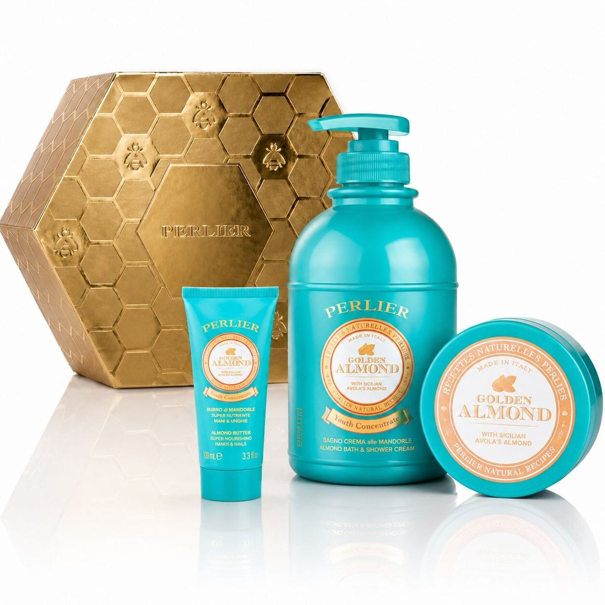 A Perlier Golden Almond gift set featuring a body wash, body balm, and hand cream, arranged in front of a gold hexagonal box on a white reflective surface.