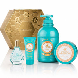 A Perlier Golden Almond gift set featuring a body wash, body balm, hand cream, and perfum, arranged in front of a gold hexagonal box on a white reflective surface.