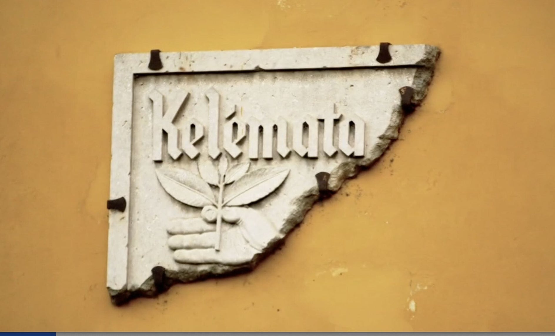 Decorative stone plaque with 'Kelimata' logo on a yellow wall