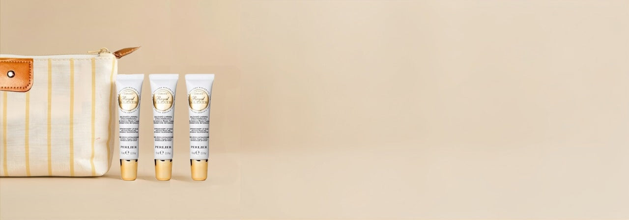 Perlier Royal Elixir Lip Balm Trio - 3 tubes of lip gloss pictured next to an off-white cosmetics bag with yellow stripes