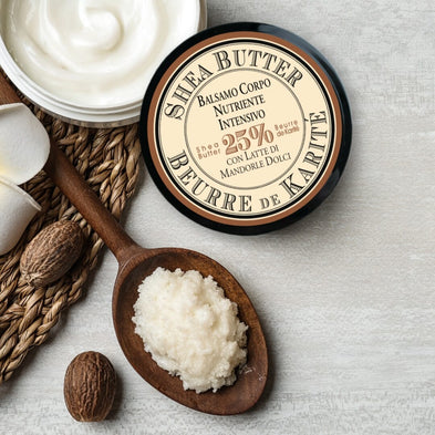 Open jar of Shea + Sweet Almond Body Balm with a wooden spoon, and raw shea butter on a textured surface